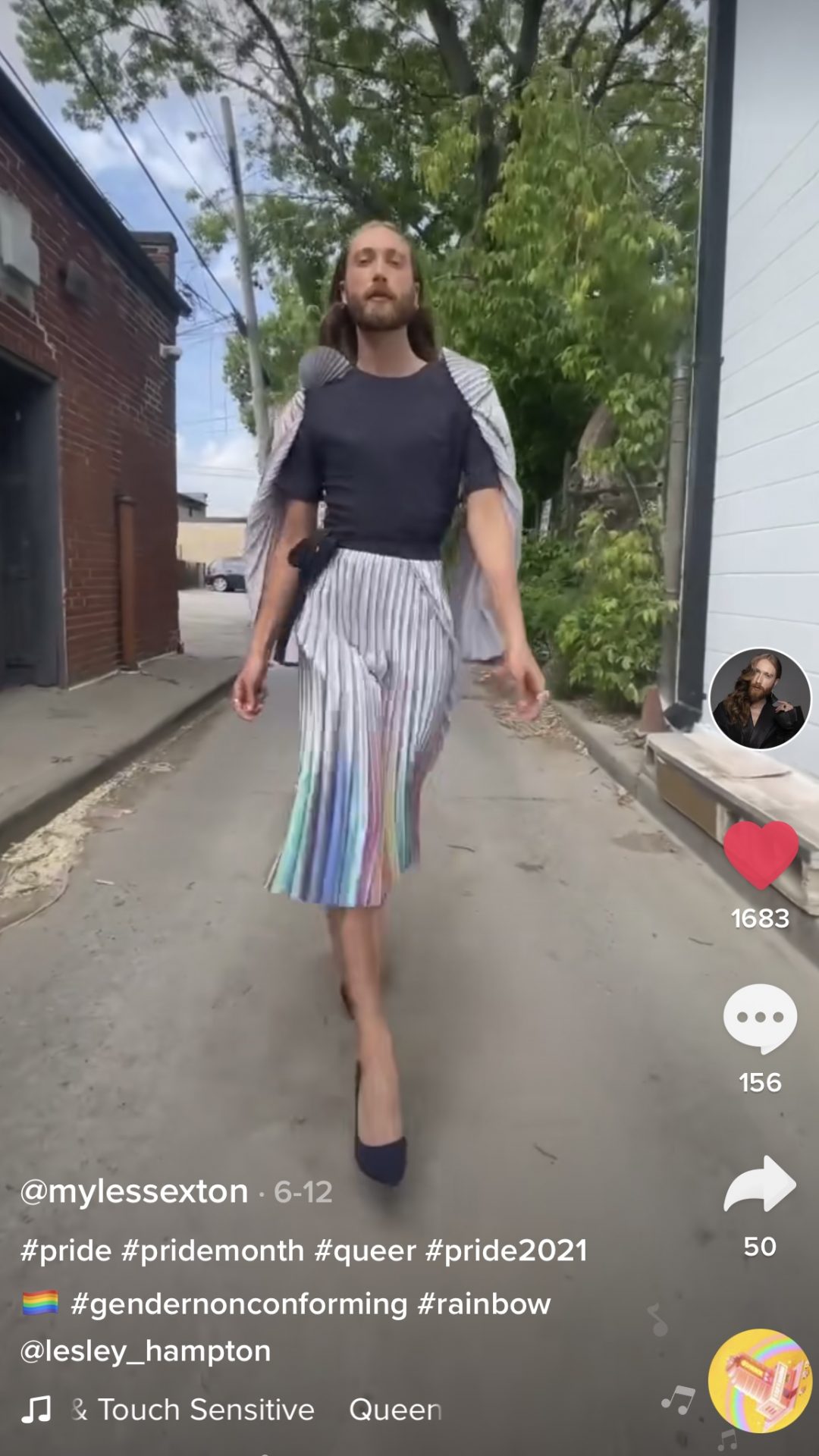 Screenshot image of a non-binary TikTok influencer wearing a black T-shirt, rainbow cape, and a matching rainbow pleated skirt with black heels walking down an alley